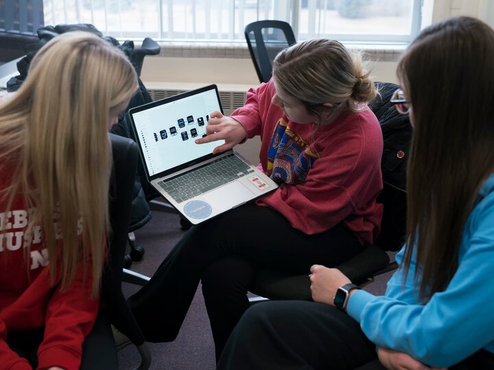 Women in a computer lab use a laptop to discuss a design project.