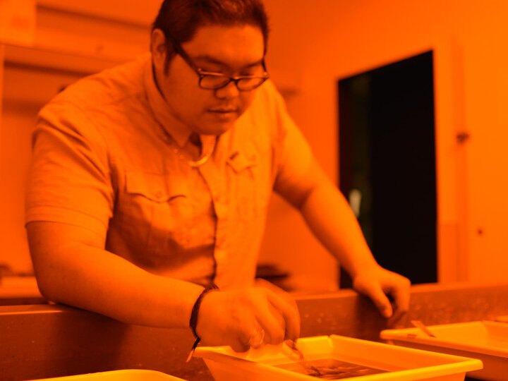 A person nudges a developing photo in a tray full of solution.