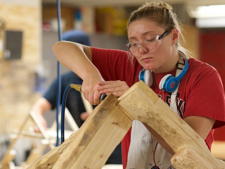A woman works with a grinding tool to rough out the form of a wood sculpture.