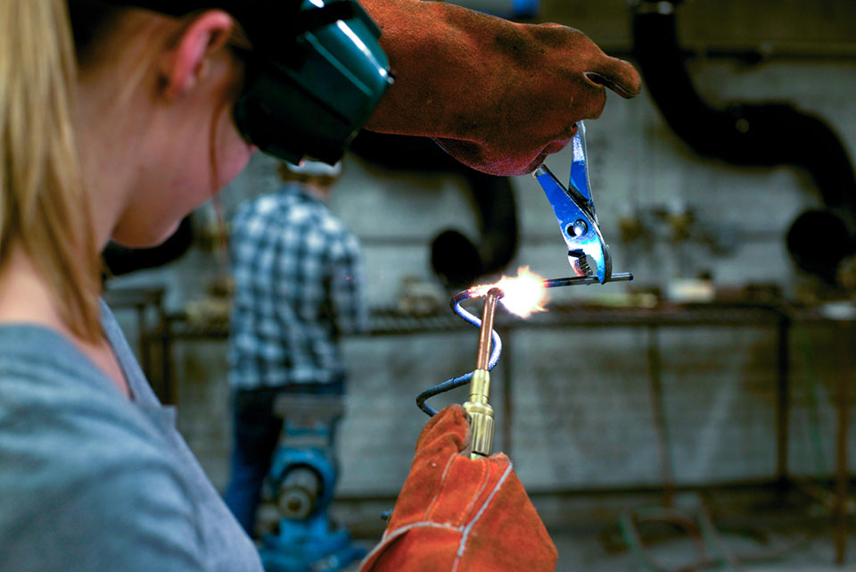 A student uses a blowtorch to manipulate metal.