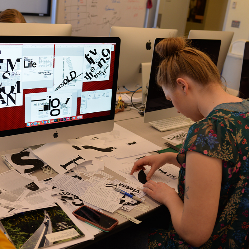 Student working on a collage project with paper and a computer.
