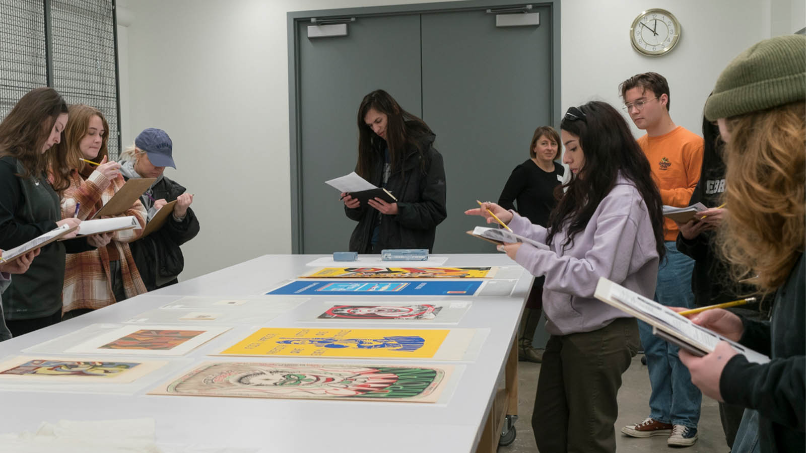 Group of people studying colorful prints on a table in a classroom setting.