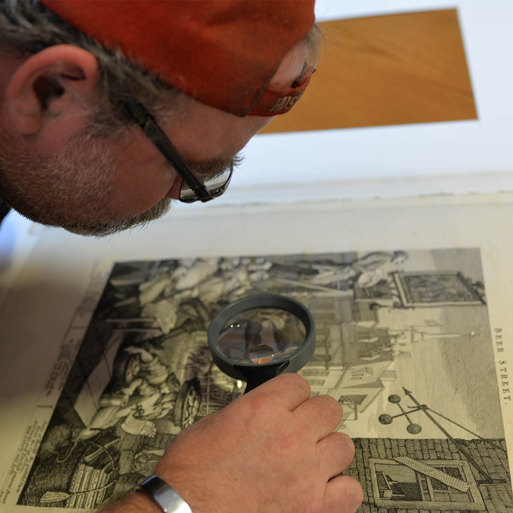 Man closely examining detailed artwork with a magnifying glass.