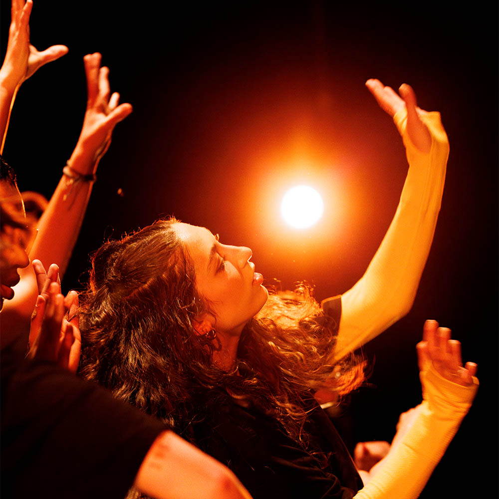 Dancers with raised arms under dramatic orange lighting.