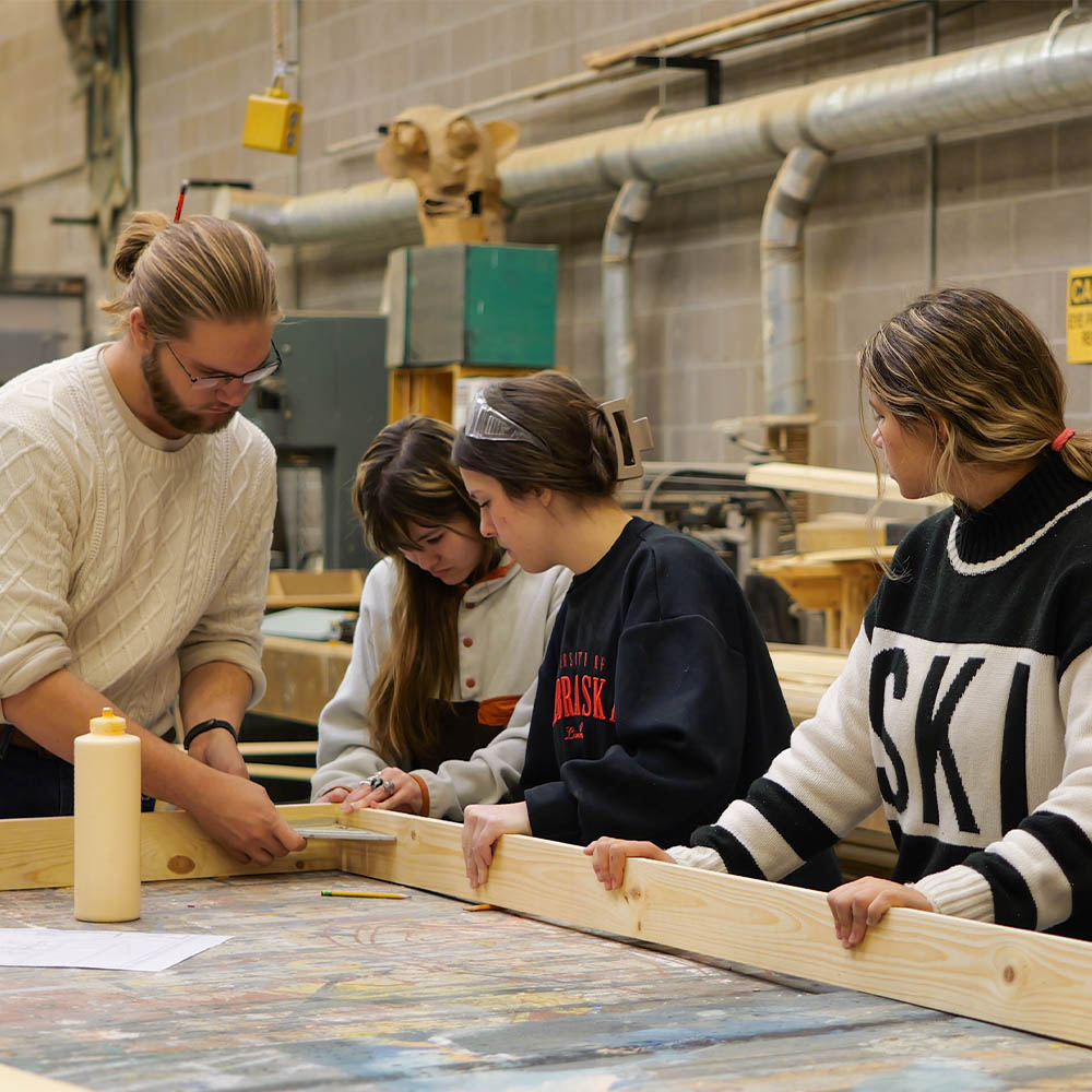 Group assembling wooden beams at a workshop table.
