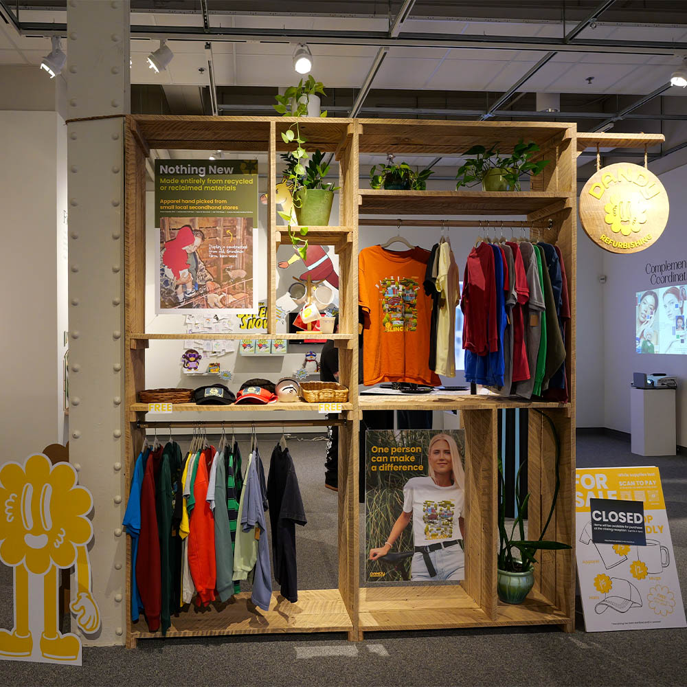 Wooden shelves displaying colorful clothing, hats, plants, and decorative signs in a retail-style setup.