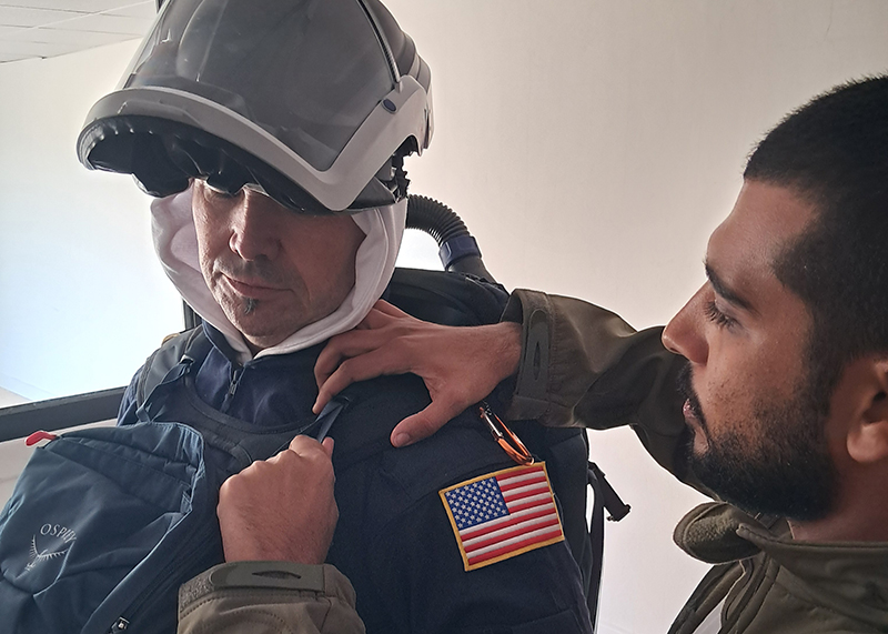 A man helps another wearing protective gear adorned with U.S. and Egyptian flag patches.