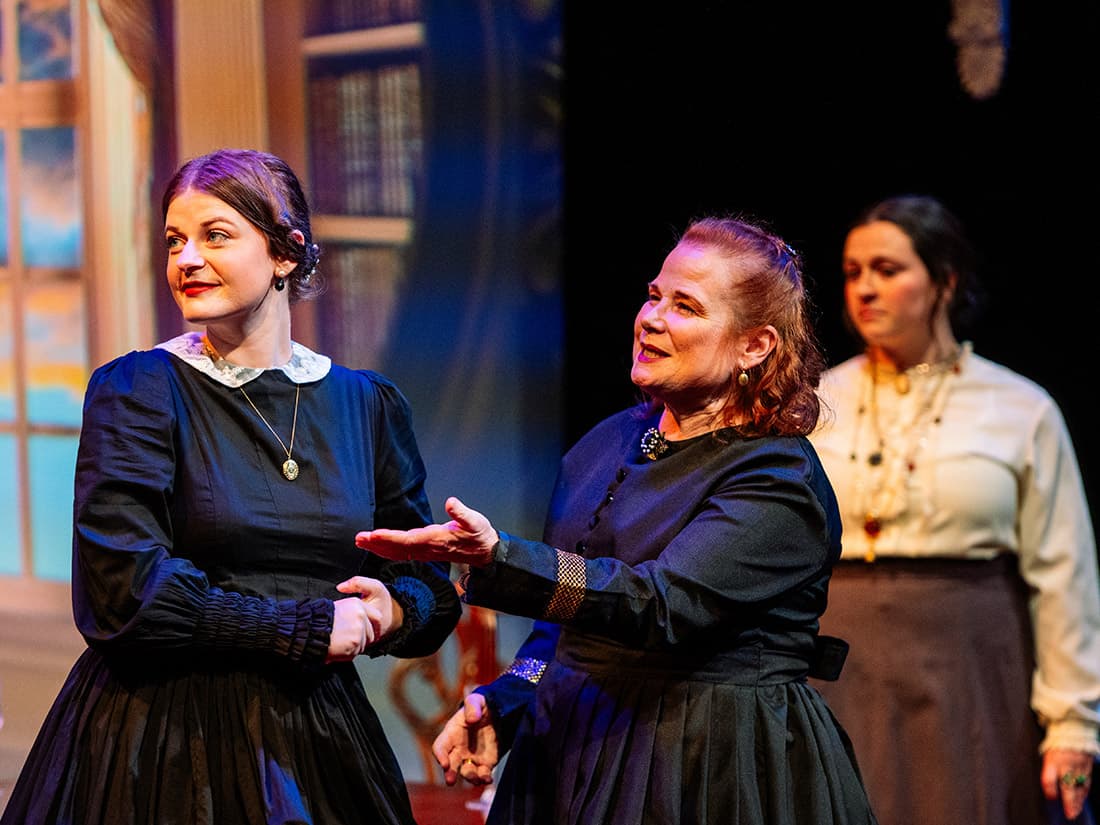 Three women in costume look offstage.