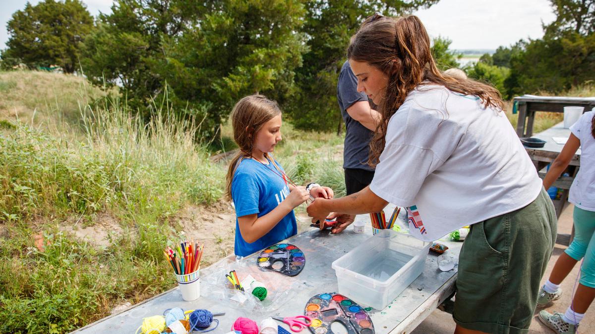 School of Art student at a table outdoors assisting a young person with painting supplies.