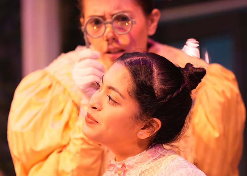 A woman look intently through a pair of spectacles at another woman.