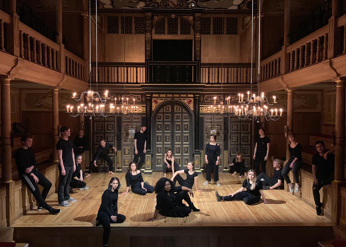 A troupe of actors pose across the stage of the historic Globe Theatre.