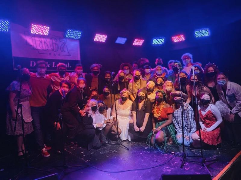 A large group of a capella signers part of UNL Boots and Cats on a stage posing for a picture.