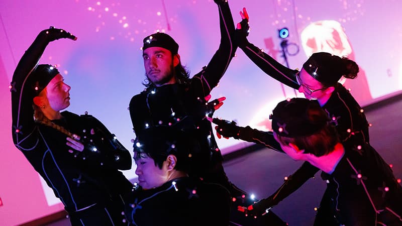 Students in the emerging media arts program pose in motion-capture suits that will help transform them into animated characters on the surrounding screen.