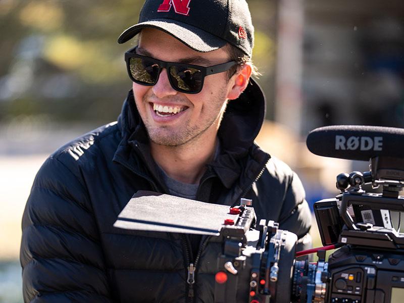 Film student alum smiling and looking off to the side while handling professional film equipment. 