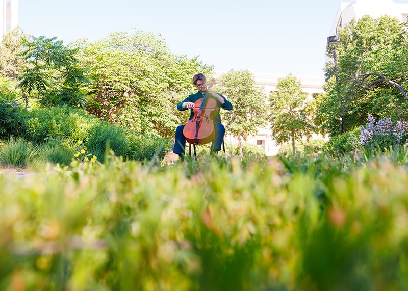 A student plays cello in a field