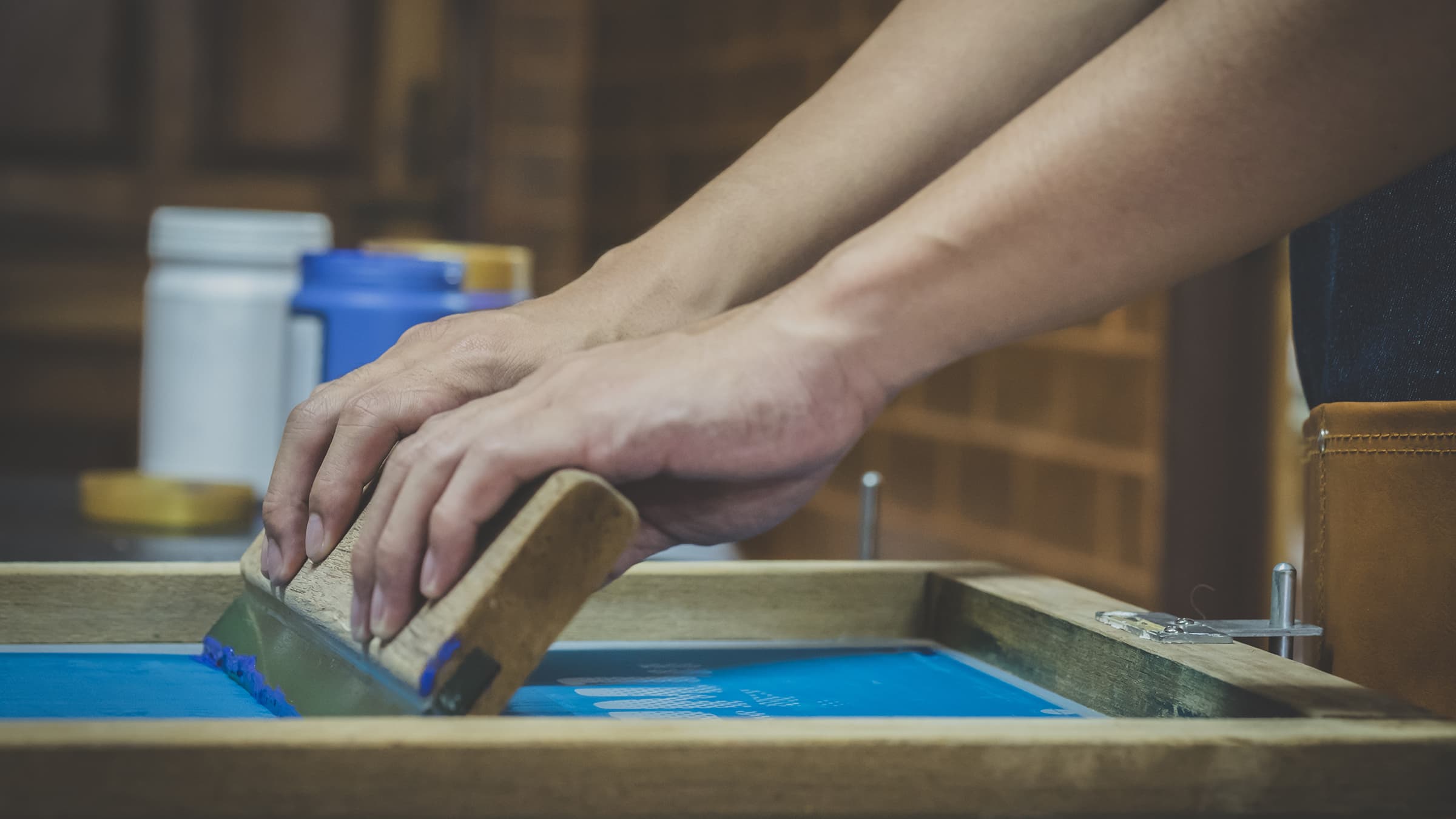 Close up of hands pulling a squeegee charged with ink across a silkscreen.