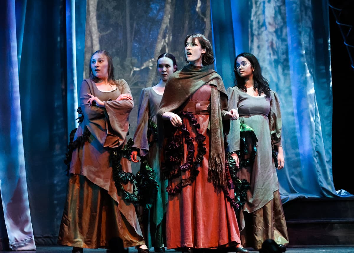 A celloist plays on stage with huge stained glass windows in the background.