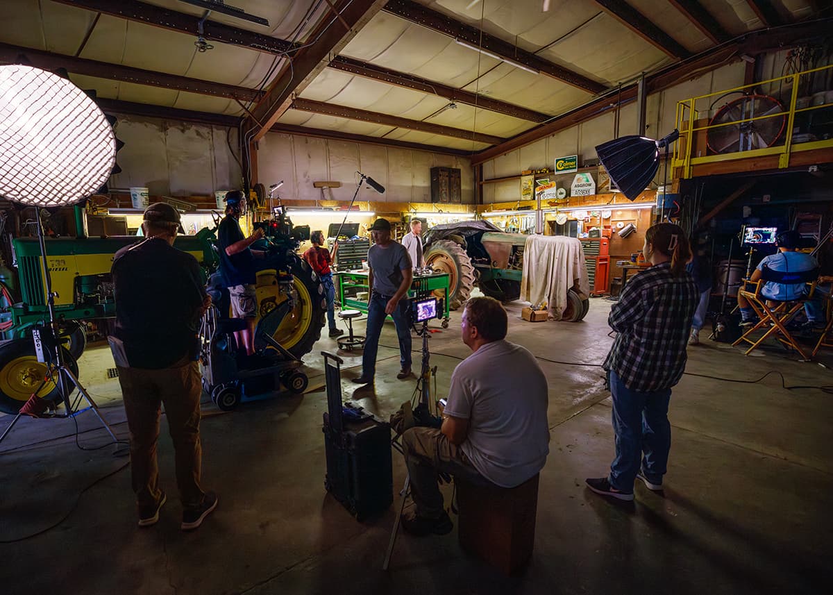 Crew members stand around a tractor in a large garage setting up a shot.