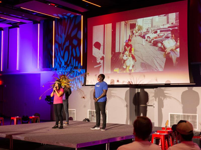 Three We Are Nebraska interns performing on a stage with a large, projected image behind them.