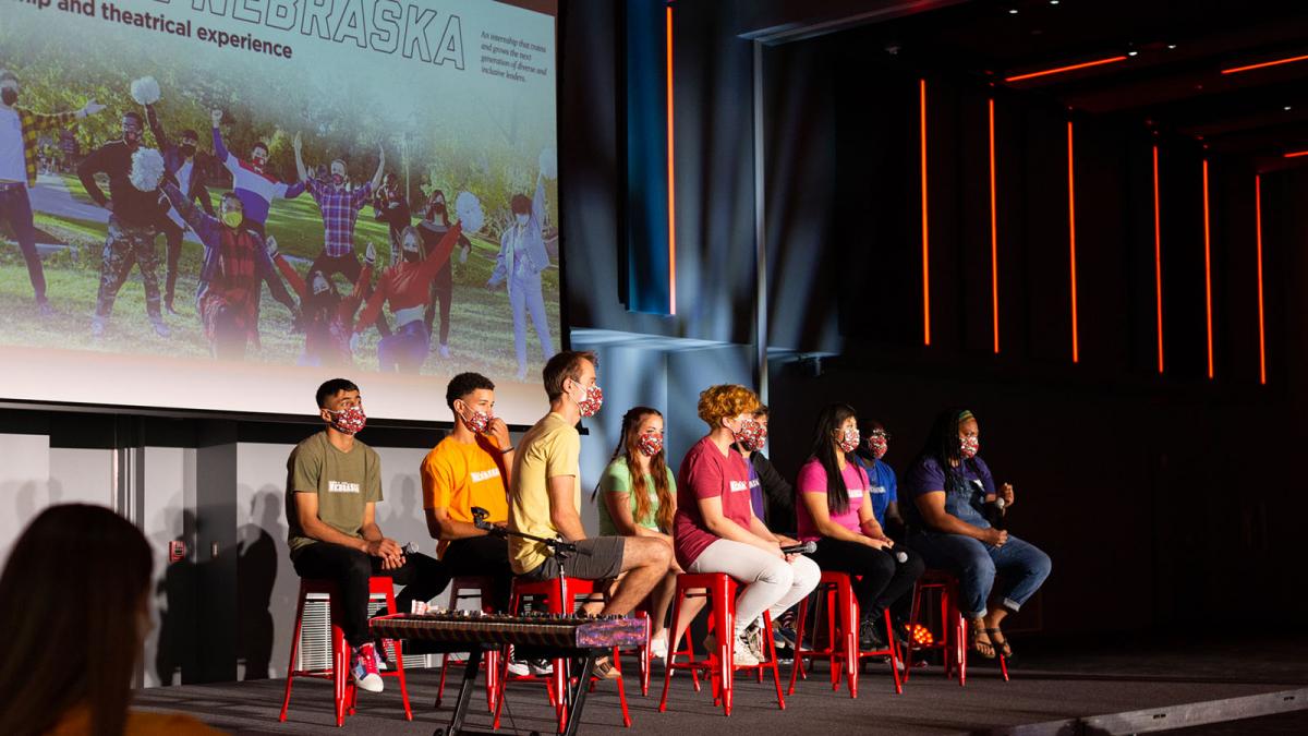 We Are Nebraska interns sitting on a stage with a large, projected image behind them looking off stage while engaging with the audience during a Q&A.