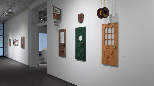 An image of a gallery wall with 3 pieces in the center and right of the frame, with a doorway separating the left side of the wall with more art pieces. 