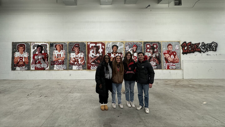 Left to right:  Michelle Reese, Maddie Vanderbur, Lea Bushey and Micah Fullinfaw stand in front of the mural they created to spotlight the players signed on National Signing Day by the Nebraska Football team. Courtesy photo.