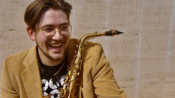 Camden Smith next to Sheldon Museum of Art with his saxophone.