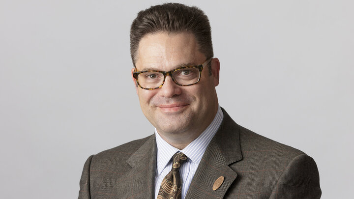 Headshot of Ora Paul Haar. He is wearing a brown suit with a red Nebraska "N" pin on it.