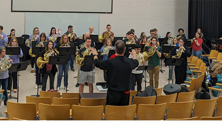 An music ensemble plays outside on the greenspace with a large sculpture in the background.