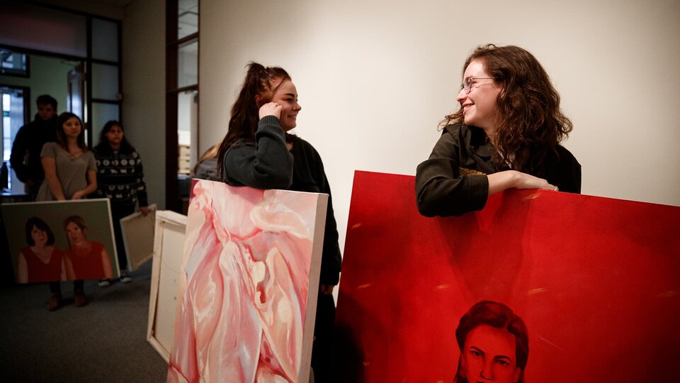 Two artists talk while holding very large painted canvases.