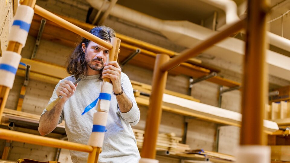 A name looks closely at a wooden project in a workshop.
