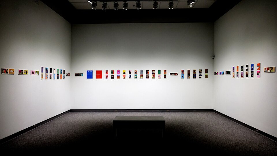 Three walls of a gallery with paintings hung in a line.