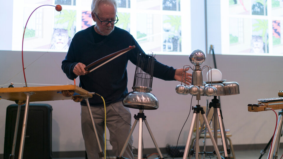 Jay Kreimer stands in front of projected images and amongst their special instruments.