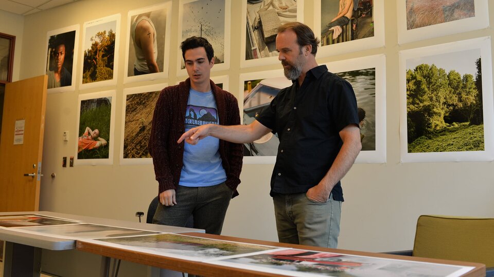 Two people talk over a table of photographs.