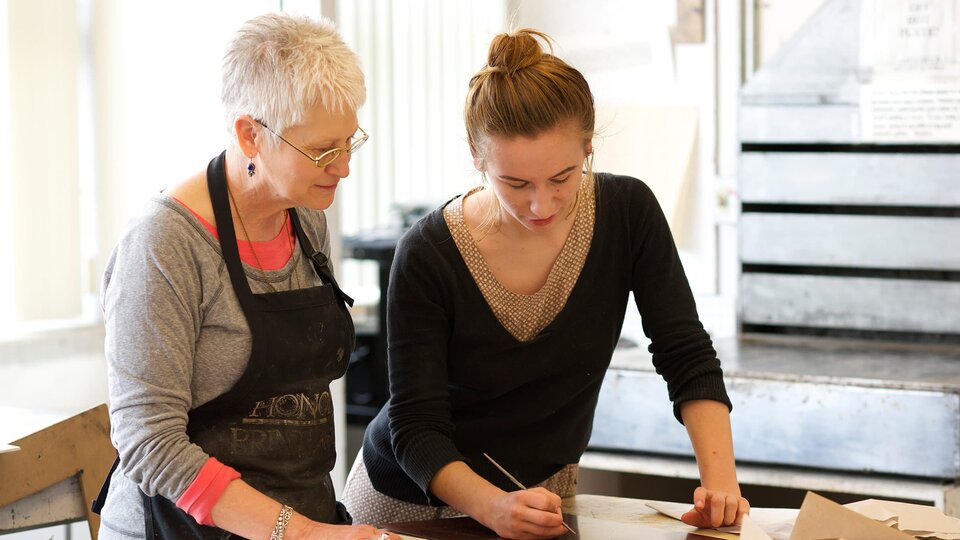 Two women look over a print in progress.