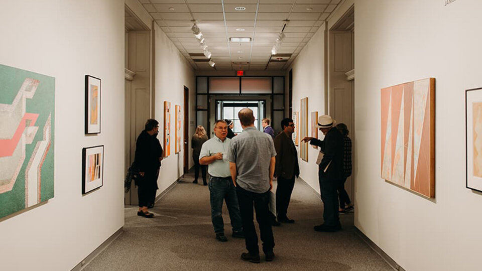 Gallery patrons stand discussing hung paintings.