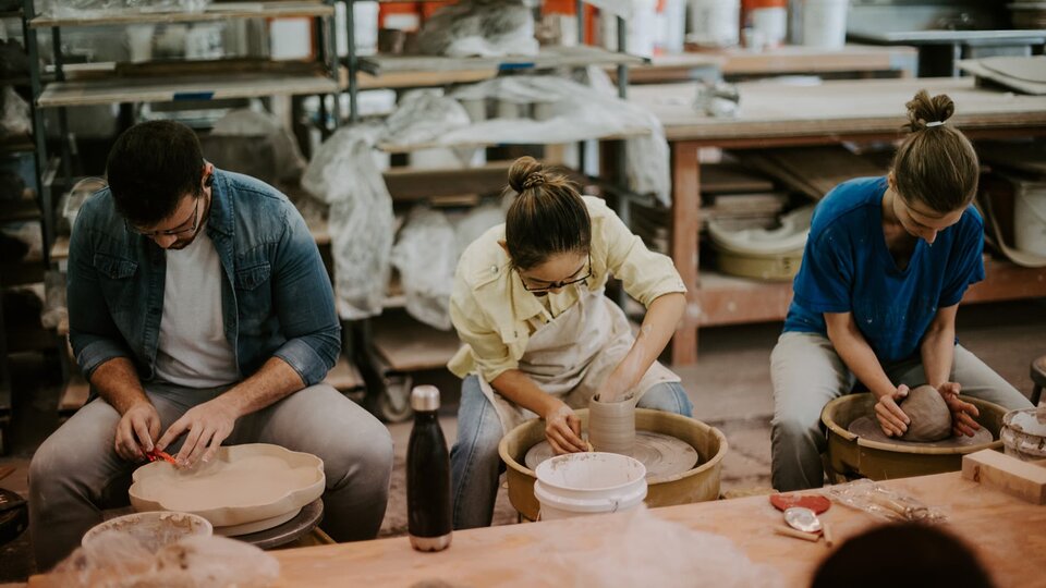 Three students work with clay on potter's wheels