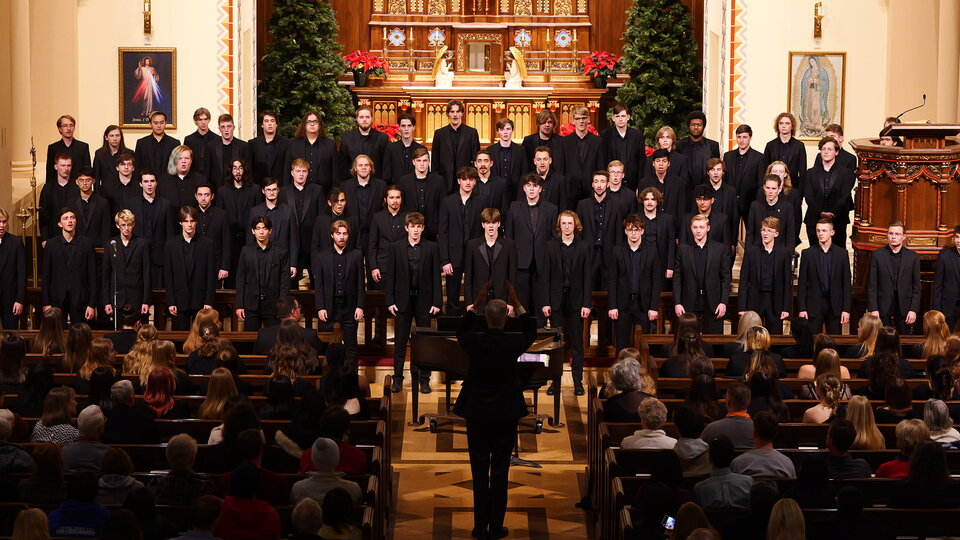 Choral singers in black suits stand in formation at the front of a church.