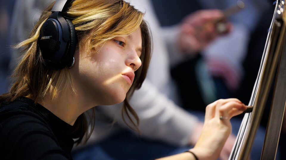 A student wearing headphones draws on an easel.