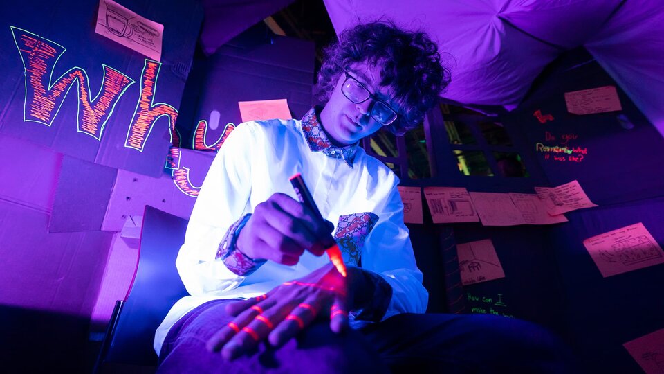A person draws on their hand with fluorescent markers under a black light.