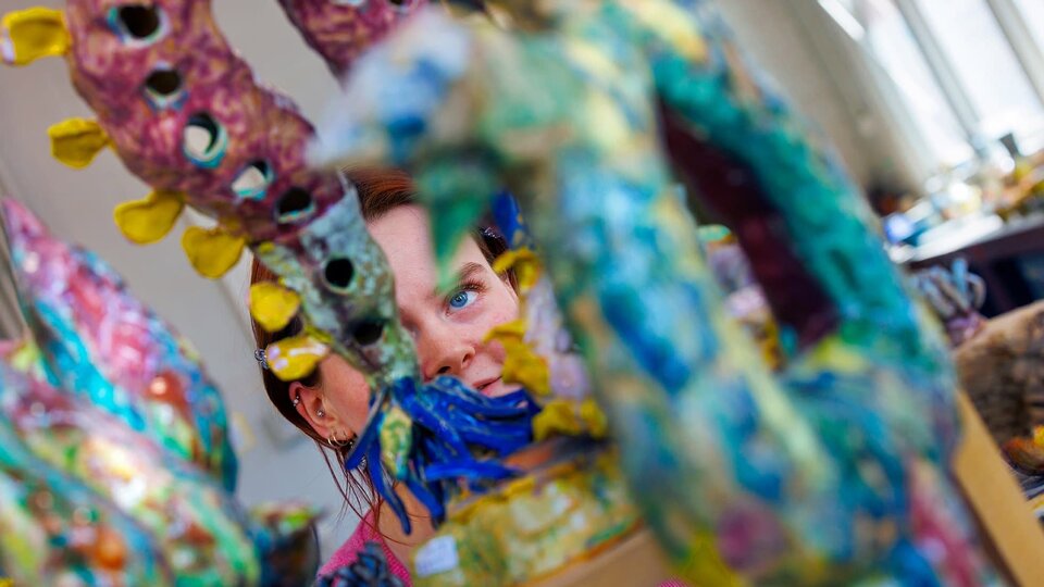 A student peaks through the openings of an elaborate ceramic sculpture.
