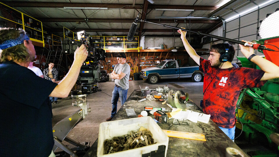 Two people hold film making equipment as a scene is being filmed.