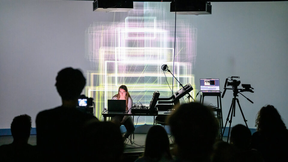 Student working on laptop in front of projection screen during open studio