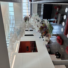 Colorful hanging sculpture in westbrook building atrium with red chairs and tables on polished floors.
