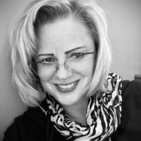 Smiling woman wearing glasses and a patterned scarf, black and white photo.