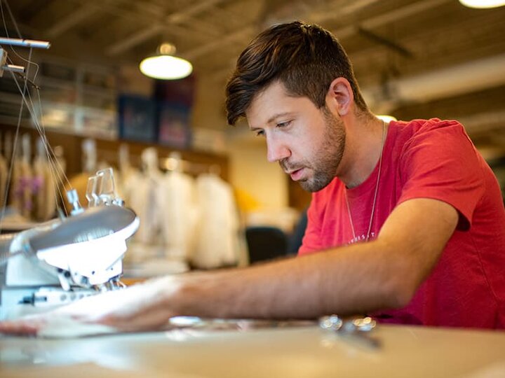 A costumer feeds fabric through a sewing machine.