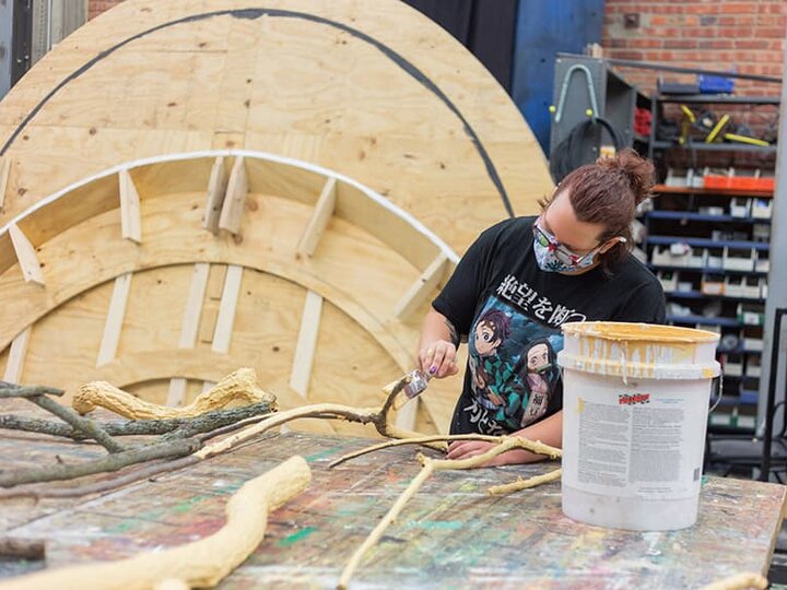 A fabricator works on a project with large unfinished set pieces in the background.
