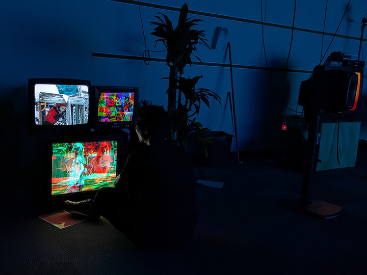 A person sits in the dark in front of three television sets.