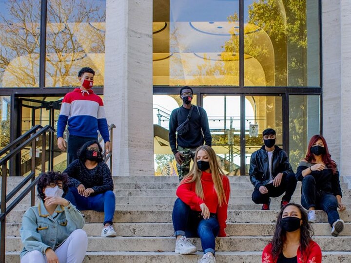 Cohort of We Are Nebraska interns sitting on the stairs leading up to Sheldon Art Museum posing in various stances for a group photo.