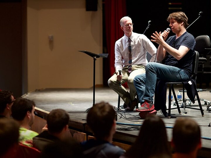 Actor Joshua Bell on stage with a Carson School professor looking out and expressively talking to an audience of theatre students